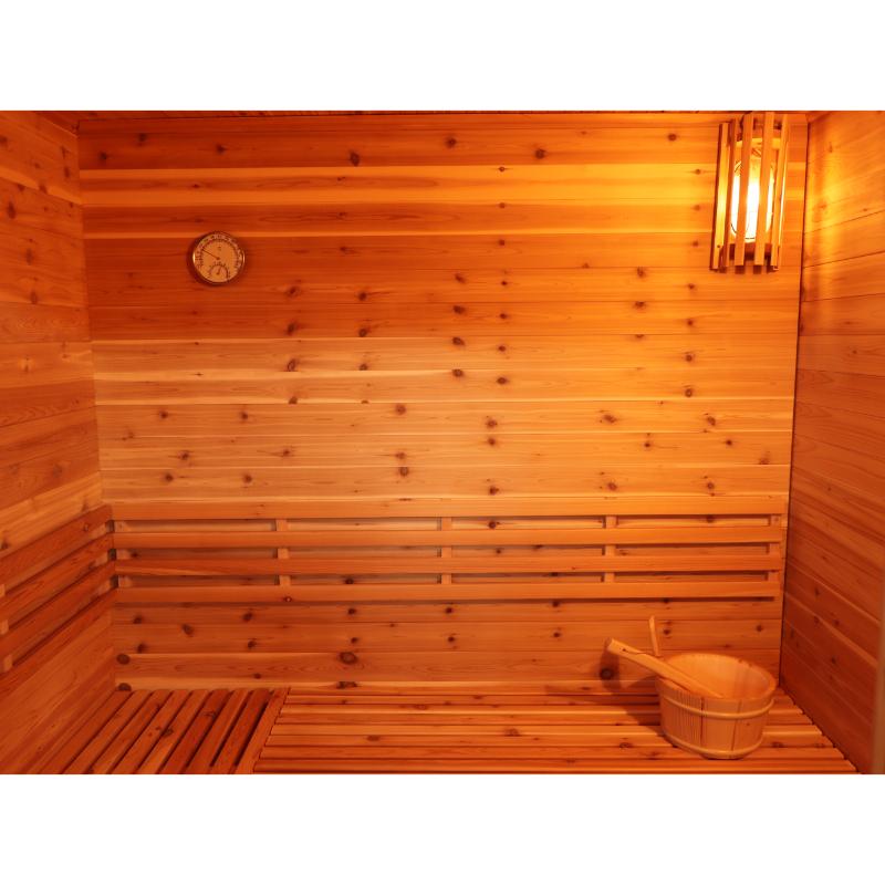 SunRay Denali HL400DS Outdoor Home Sauna - interior view of the bench with bucket and ladle to the bottom right, the interior light illuminated at the top right and the hygrometer on the wall to the top left.