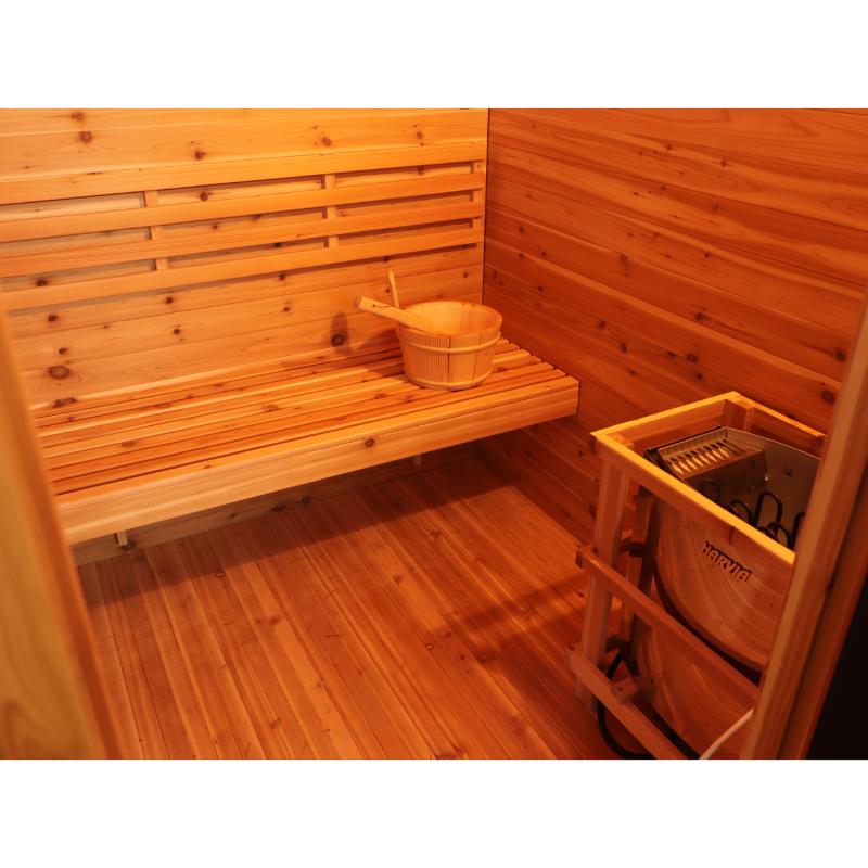 SunRay Denali HL400DS Outdoor Home Sauna - interior view of the sauna bench with bucket and ladle to the right, the sauna heater without rocks sitting to the right.