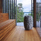 12 kW Electric Sauna Heater - the sauna heater sitting on the floor of a sauna with 2 perpendicular glass walls and a view of a lake in the distance and trees 