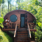 Sauna Life G11 Dome Outdoor Home Sauna - Exterior straight front view, sauna is elevated with stairs leading up to the porch, A lady sitting on the porch and the sauna door is open.