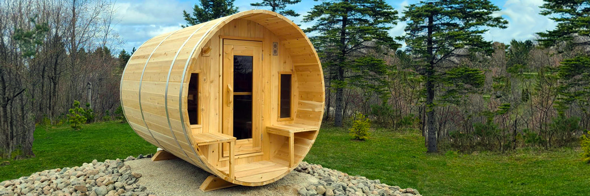 Sauna DIY Kits with Free Shipping - this is a barrel sauna outdoors in nature, looking rustic and natural for a backyard, by the cabin or by the lake. This has a front porch and two side windows beside the door with a glass panel.