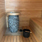 HIVE Mini Series 10.5kW Sauna Heater - the sauna heater sitting on the floor of the sauna with a bucket and ladle beside it and next to sauna benches