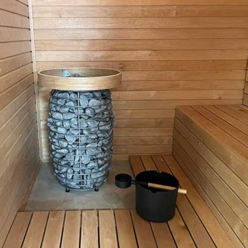 HIVE Mini Series 10.5kW Sauna Heater - the sauna heater sitting on the floor of the sauna with a bucket and ladle beside it and next to sauna benches