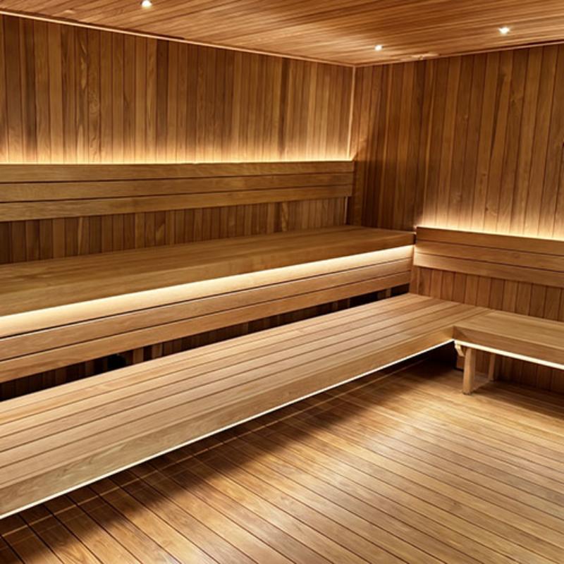 A wooden sauna interior with tiered seating, wood-paneled walls, and warm under-lighting.
