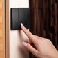 A close-up of a black three-button wall switch being pressed by a hand with a French manicure, set against a light wood panel and a dark brown textured background.