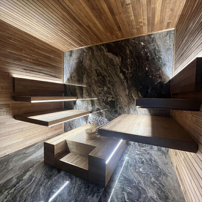 Modern sauna interior with tiered wooden benches and marble floor and one marble wall